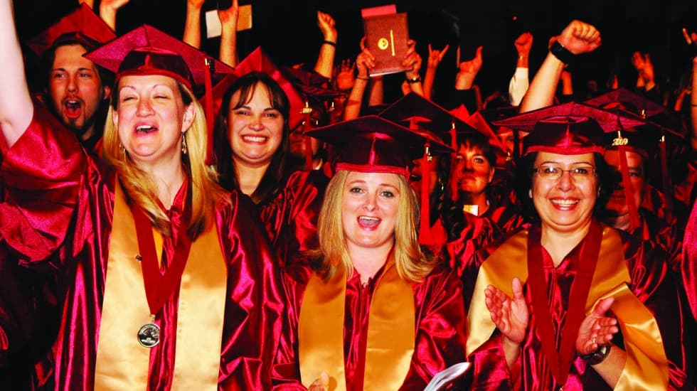 PCC graduates in maroon gowns and gold stoles cheer at commencement