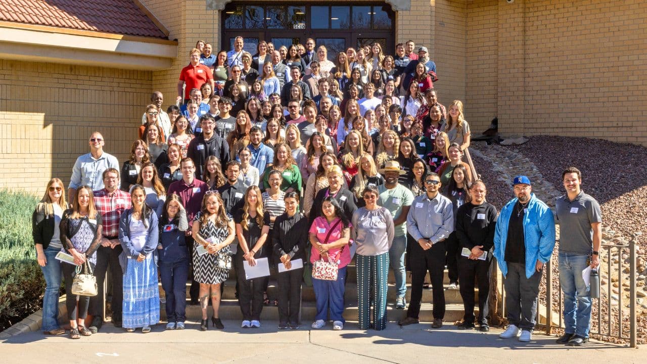 More than a hundred PCC Foundation scholars and donors, many holding certificates, gathered on the steps of a tan-brick Pueblo Community College building